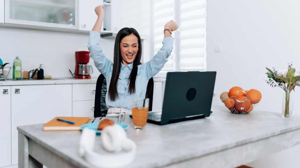 Cheerful woman celebrating victory at home office desk.